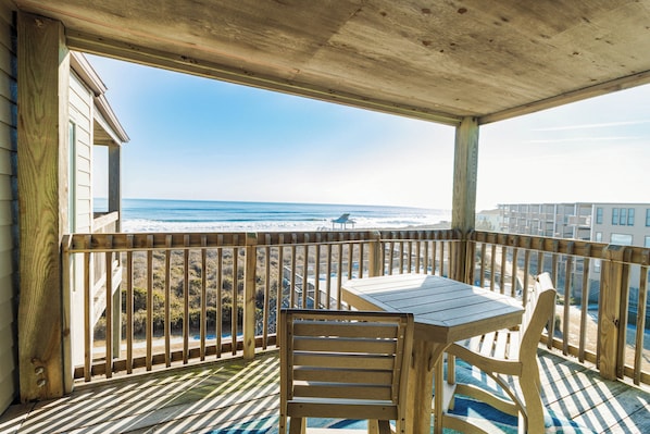 A wooden deck with a table and chairs overlooking a beach. - Oceanfront condo with great views & community pool! (Duck)