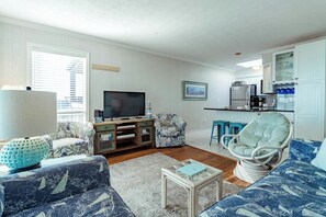 Una sala de estar con televisor, asientos, una mesa de centro y una cocina con taburetes de bar.