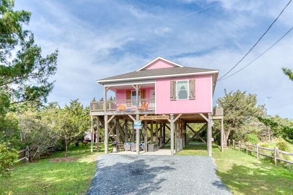 A pink house with a balcony, a sign reading "Barbie's World," and a gravel path leading to it.