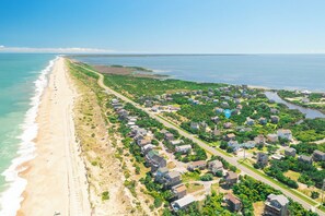 An aerial view of a coastal residential area with houses, a beach, and a road running parallel to the shore.