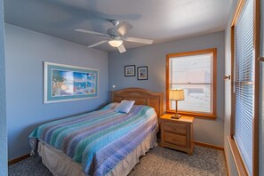 Un dormitorio con cama, mesita de noche, ventilador de techo y ventana con persianas.