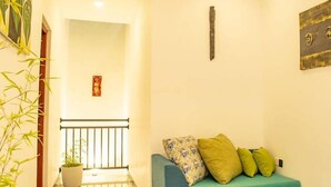 A modern living room with a blue sofa, green cushions, a potted plant, and a decorative wall piece.