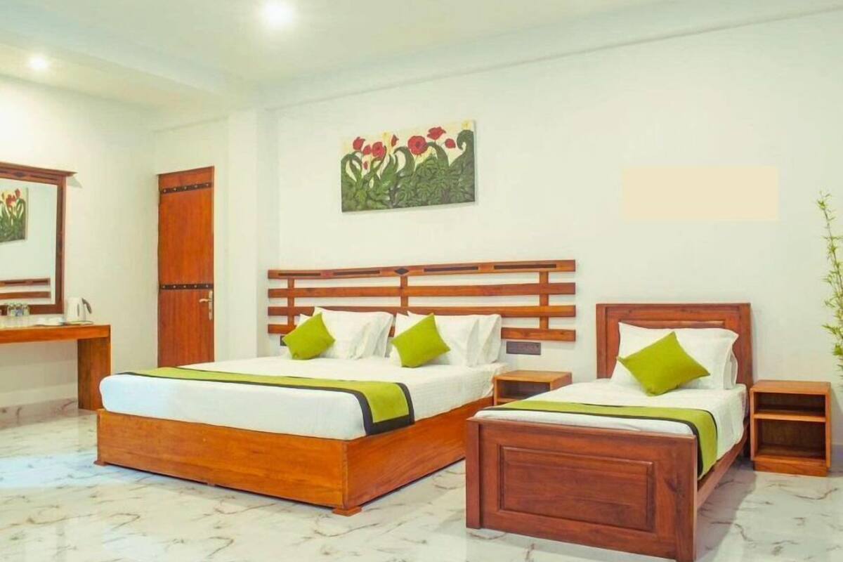 A hotel room with a large bed, two bedside tables, a wooden wardrobe, and a painting on the wall.