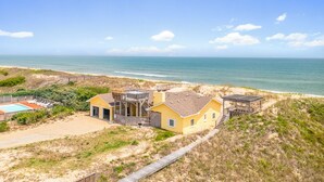 A coastal property with a large house, a swimming pool, and a beach view.