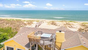 A beachfront property with a wooden deck, a hot tub, and a view of the ocean.