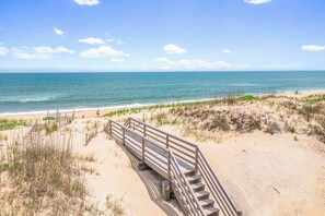 A wooden boardwalk leading to a sandy beach with the ocean in the background.