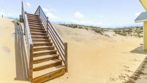 A wooden staircase leading to a sandy beach area with a small yellow building in the background.