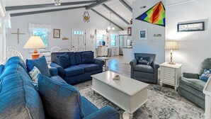 A spacious living room with a high ceiling, a dining area, and a kitchen in the background.