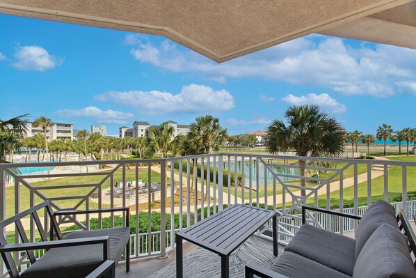 A balcony with a view of a pool, palm trees, and a building complex.