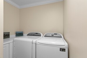 A laundry room with two front-loading washing machines and a dryer. - Amalfi Coast 209A - Gulf View, Swimming Pool, Tennis Court, Near Shops + Dining! (Miramar Beach)