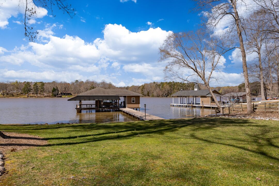 A lakeside property with a dock, a covered outdoor seating area, and a small building.