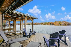 Een houten terras met Adirondack-stoelen met uitzicht op een meer, omringd door herfstbomen.