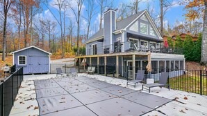 A two-story house with a covered patio area, a small shed, and a large deck with outdoor furniture. - Hot Tub, Boat Dock, Large Deck, Firepit, Tiki bar, Pool! (Littleton)