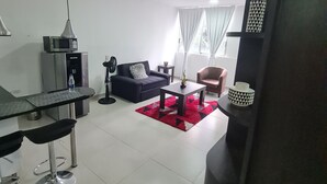 Ein modernes Wohnzimmer mit einer schwarzen Couch, einem Teppich in Rot-Weiß-Muster, einem Essbereich mit Barhocker und einer schwarzen Akzentwand.
