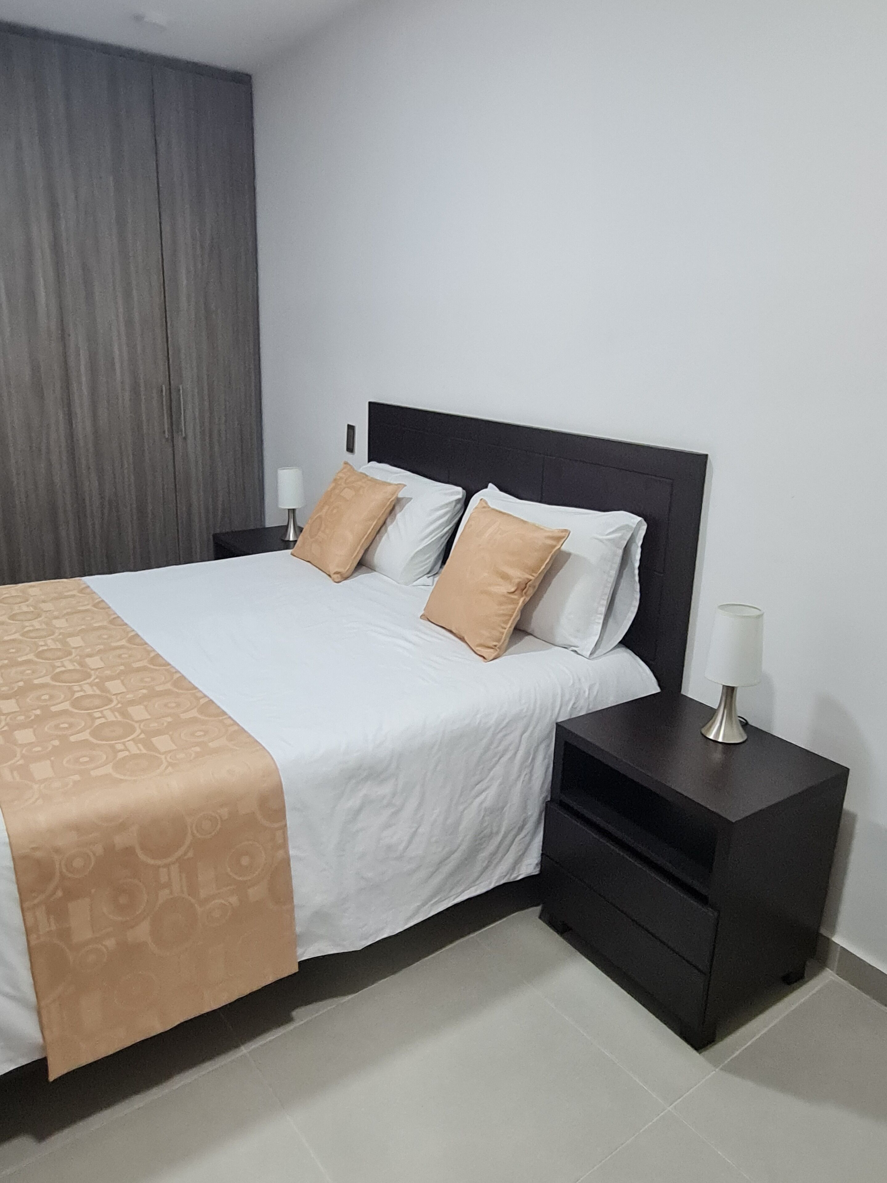 A neatly made bed with a patterned bedspread, two pillows, and a bedside table with a lamp.