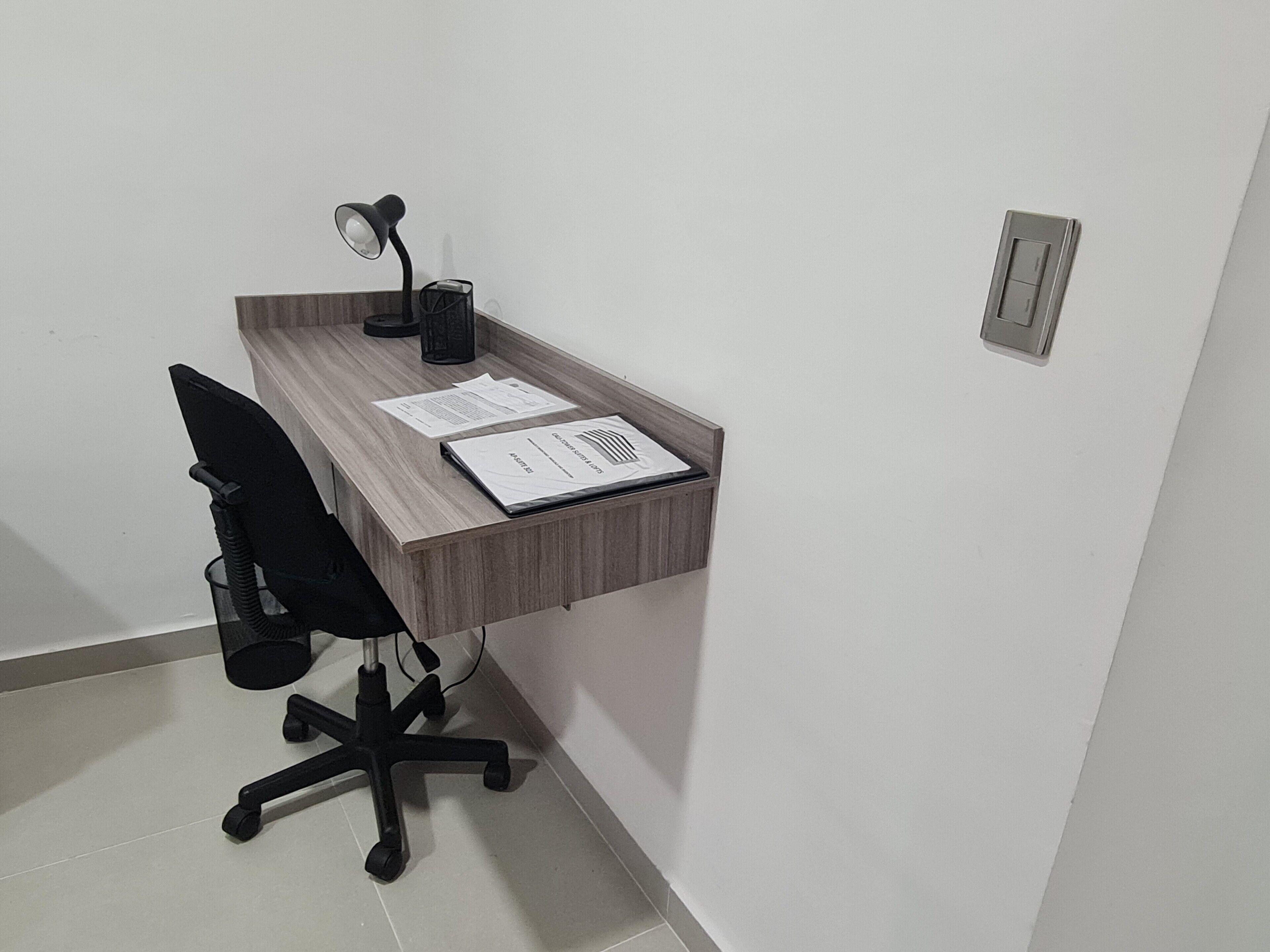 A small office space with a desk, chair, lamp, and papers.