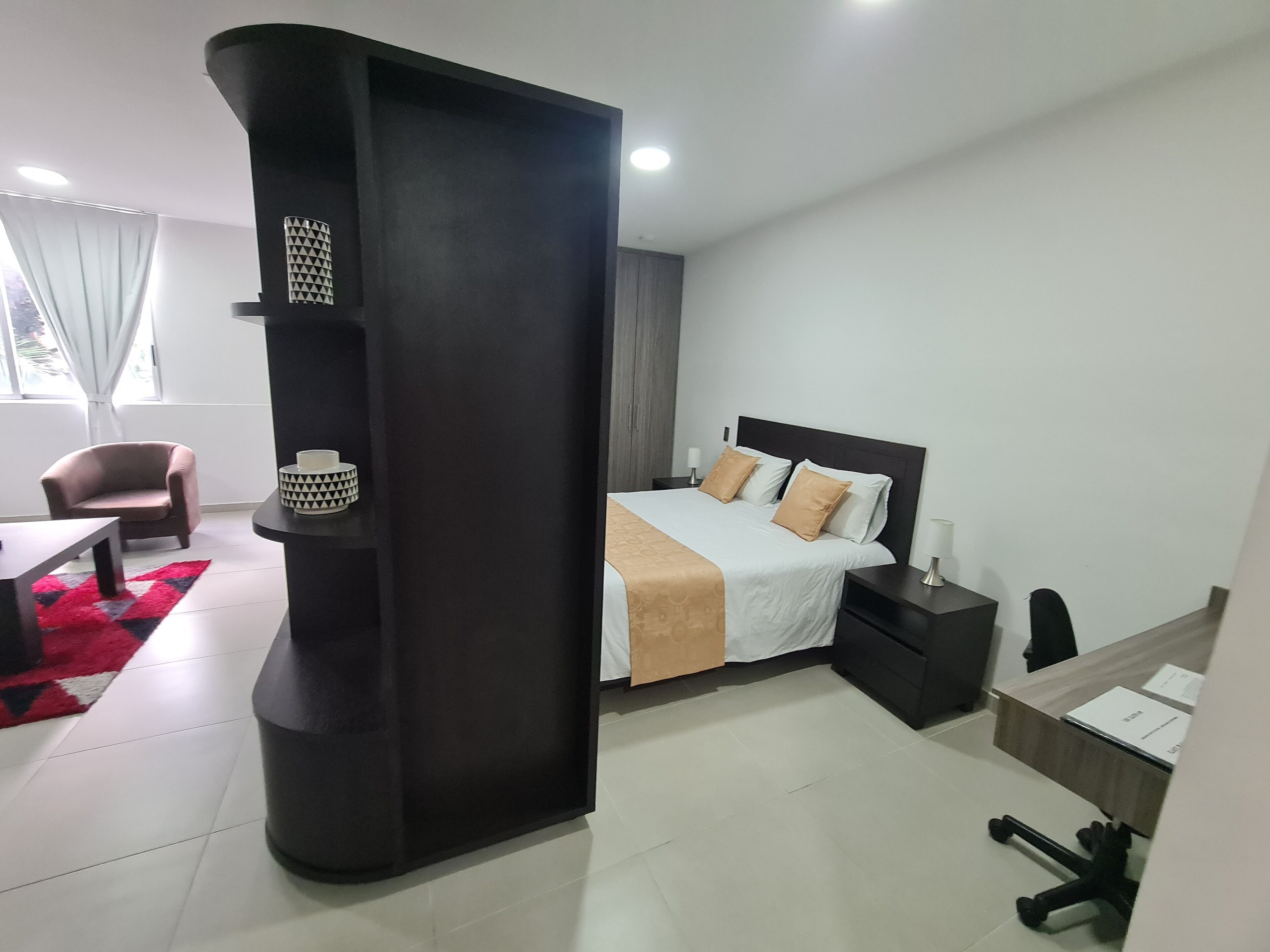 A modern hotel room with a bed, bedside tables, a chair, and a desk.