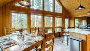 A wooden cabin with a dining area and kitchen, large windows, and a high ceiling. - Game Room | Scenic Views | Cozy Fireplace (Grand Lake)