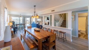 A spacious dining area with a wooden table and benches, a chandelier, and a view of a staircase leading to a second floor. - Gorgeous pet-friendly oceanfront duplex in Nags Head w/ a hot tub & rec room (Nags Head)