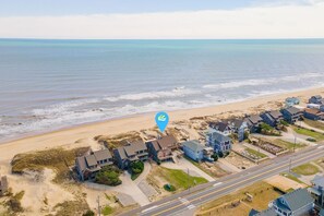 An aerial view of a coastal residential area with houses near the beach, a road, and a blue location marker.