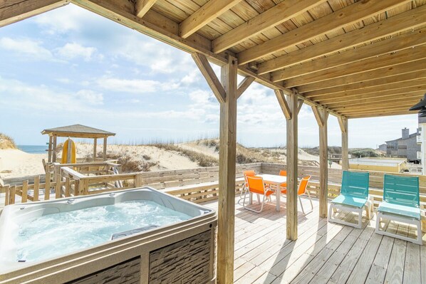 A wooden deck with a hot tub, outdoor seating, and a view of the beach.
