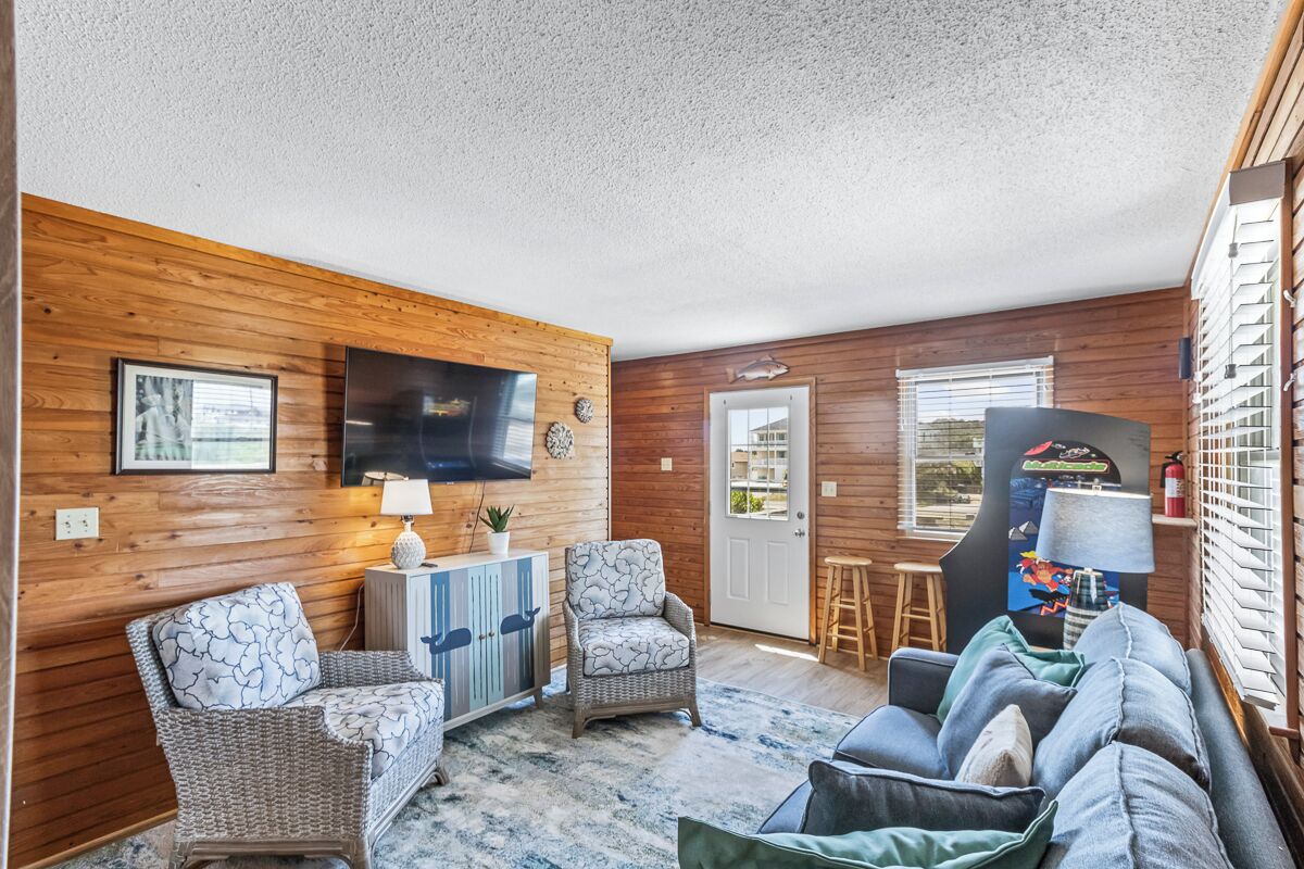 A cozy room with wooden walls, a flat-screen TV, wicker furniture, and a sofa with pillows.
