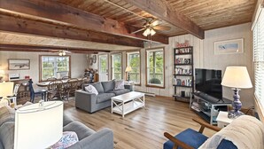 A spacious living room with wooden beams, a grey sofa, a coffee table, a TV, and a bookshelf. - Semi oceanfront home in Salvo w/ beach access just across the street! (Salvo)