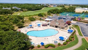 A residential area with a large swimming pool, tennis courts, and a golf course in the background.