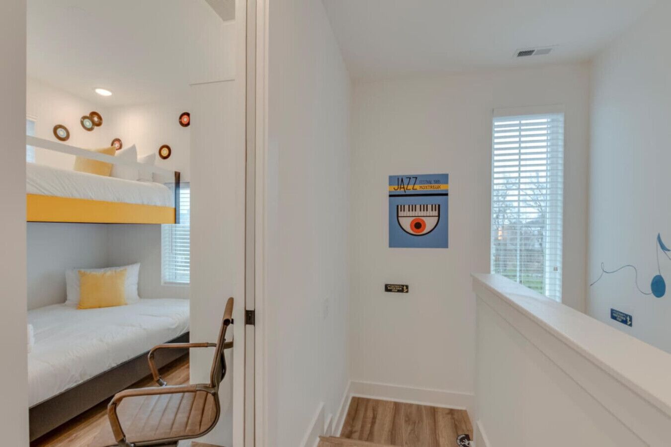 A room with bunk beds, a wooden chair, a window with blinds, and a wall with a poster.