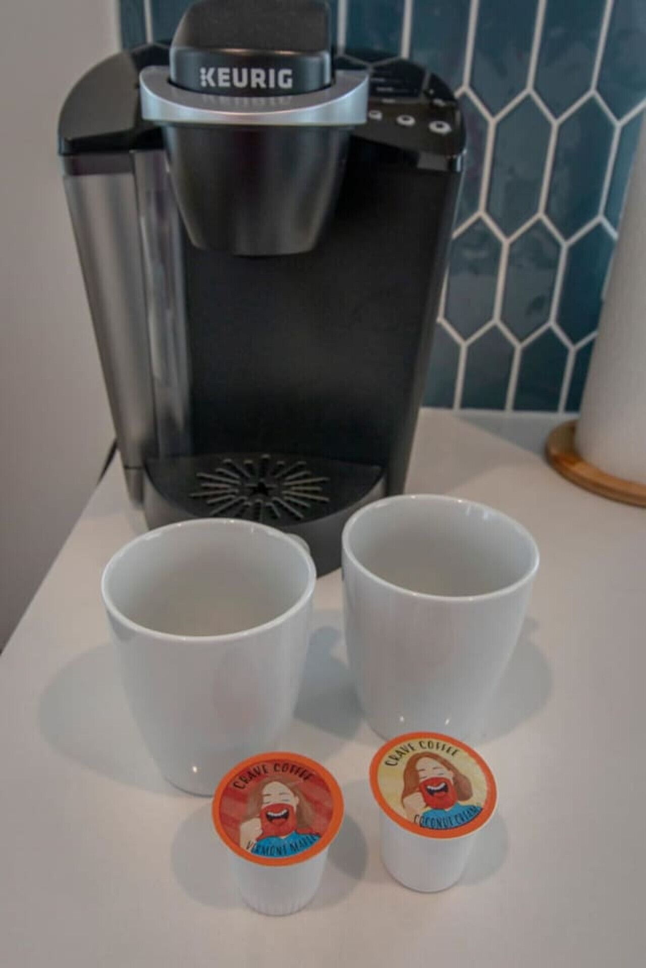 En Keurig kaffemaskine med to hvide kopper og to låg med kaffemotiver.