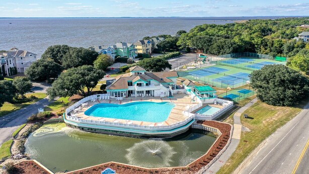 Une grande piscine entourée d’une terrasse, de courts de tennis et offrant une vue sur la mer.