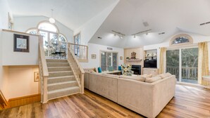 Un vaste espace de vie doté d’un plancher en bois, d’un canapé beige, d’un escalier et d’un coin cuisine avec un téléviseur.