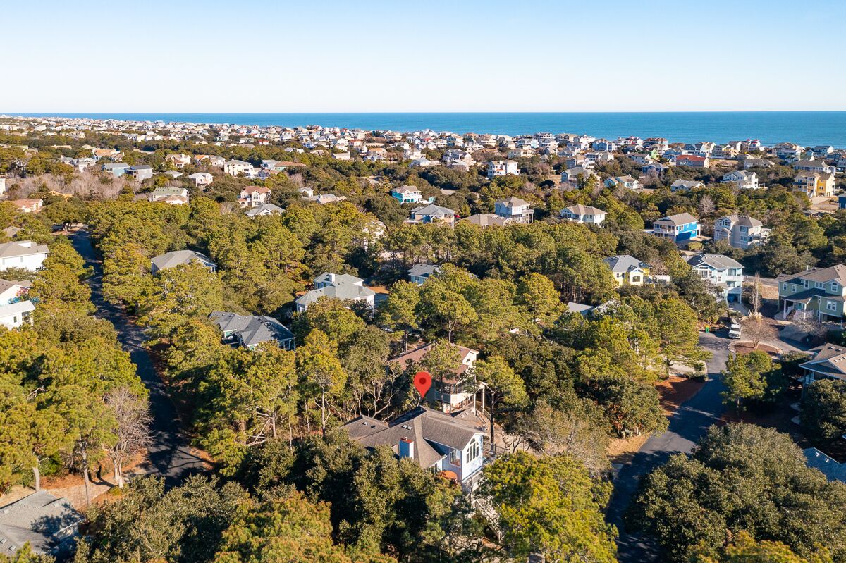 Une vue aérienne d’un quartier résidentiel, avec des maisons entourées d’arbres, un ciel dégagé et une vue sur l’océan au loin.