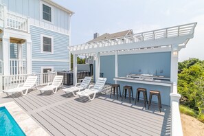 Relax on the deck with lounge chairs and bar stools, surrounded by lush greenery and a small pool.