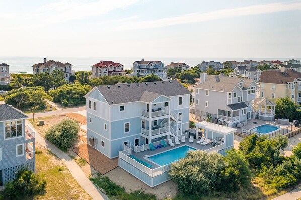 Enjoy ocean views from the two-story house's spacious balcony and backyard, featuring a swimming pool surrounded by lush greenery.