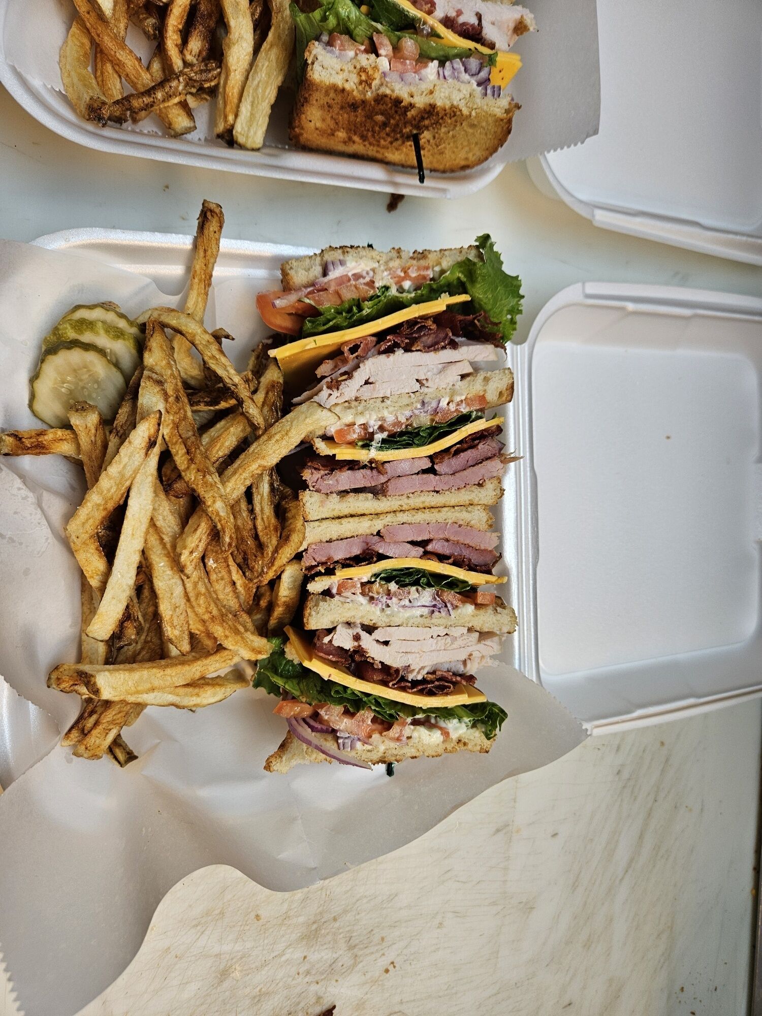 A meal consisting of a sandwich and fries in a takeout container.