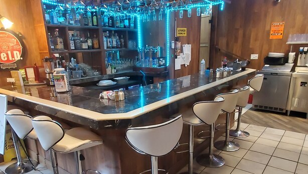 Un espace bar avec un comptoir, des tabourets et des étagères remplies de bouteilles.