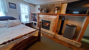 Une chambre à coucher avec un lit à baldaquin, une cheminée en pierre, une télévision et une petite table avec une lampe.