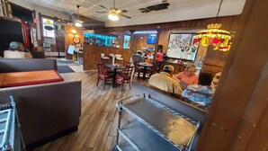 L’intérieur d’un restaurant, avec un plancher en bois, des tables, des chaises, un bar et un ventilateur de plafond.