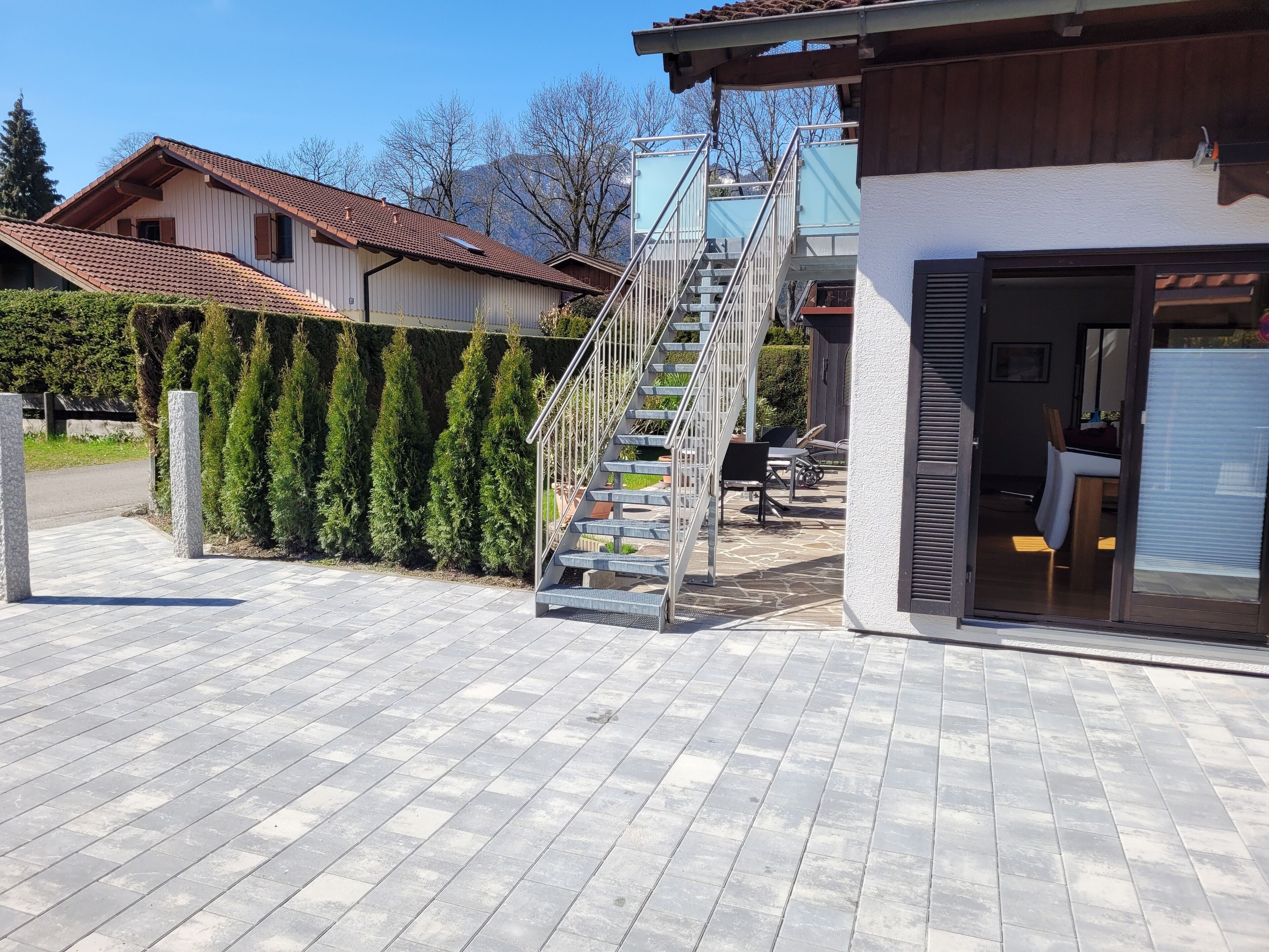 A residential property with a staircase leading to a second floor, a covered outdoor seating area, and a garage door.