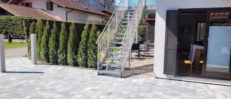 A residential property with a staircase leading to a second floor, a covered outdoor seating area, and a garage door.