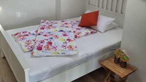 Een net opgemaakt bed met een bloemenbedekker, een rood kussen en een klein houten tafeltje met een vaas.