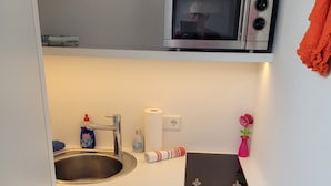 Een kleine keuken met een roestvrijstalen spoelbak, een magnetron, en een klein aanrecht met een keukenrol en een fles afwasmiddel.