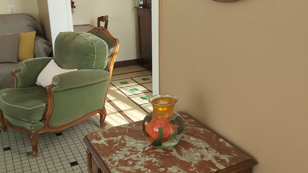 Ein Zimmer mit einem grünen Sessel, einem Holzschrank, einer Blumenvase und einem Gemälde an der Wand.