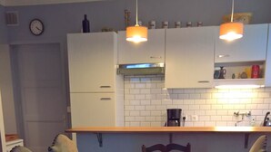 Ein Esstisch mit vier Stühlen, eine Küchenzeile mit weißen Schränken und einer gefliesten Rückwand, sowie eine Uhr an der Wand.