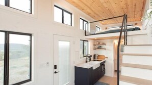 A modern interior with a kitchen, a staircase, and a view of the outdoors. - Tiny Home Near Palo Pinto Mountains State Park + Scenic Views + Fire pit + Grill (Ranger)