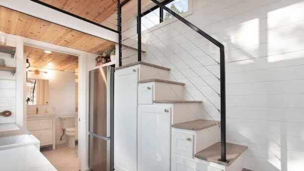 Una cucina compatta con mobili bianchi, frigorifero integrato e soffitto in legno.