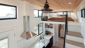 Una moderna camera da letto su più livelli con una cuccetta, una cucina con lavello e pensili, e ampie finestre che offrono vista sull'esterno.