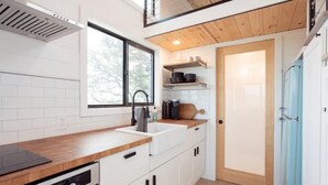 Une cuisine moderne avec des armoires blanches, un plan de travail en bois, une cuisinière intégrée et une fenêtre qui laisse entrer la lumière naturelle.