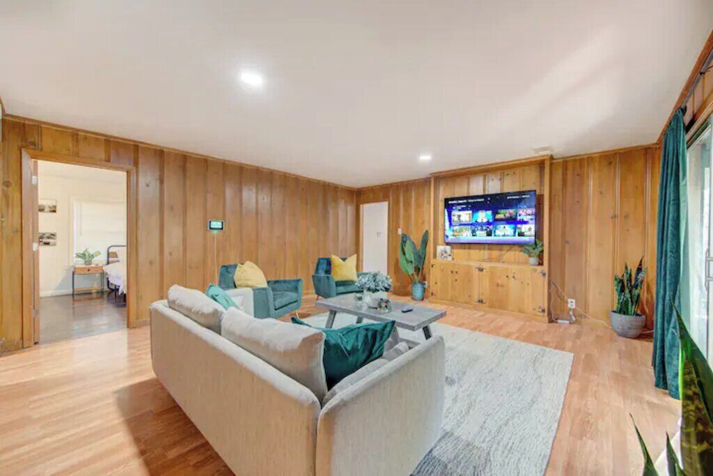 Un amplio salón con paneles de madera, un televisor de pantalla plana grande, un sofá, sillones y una mesa de centro.